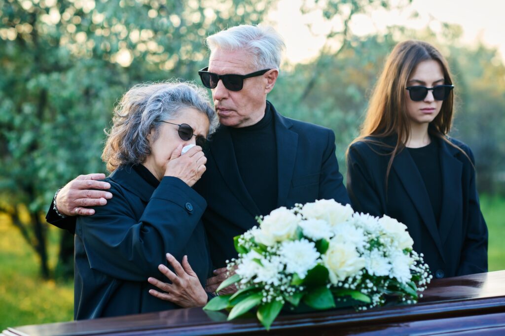 Mature man in black attire and sunglasses consoling his wife